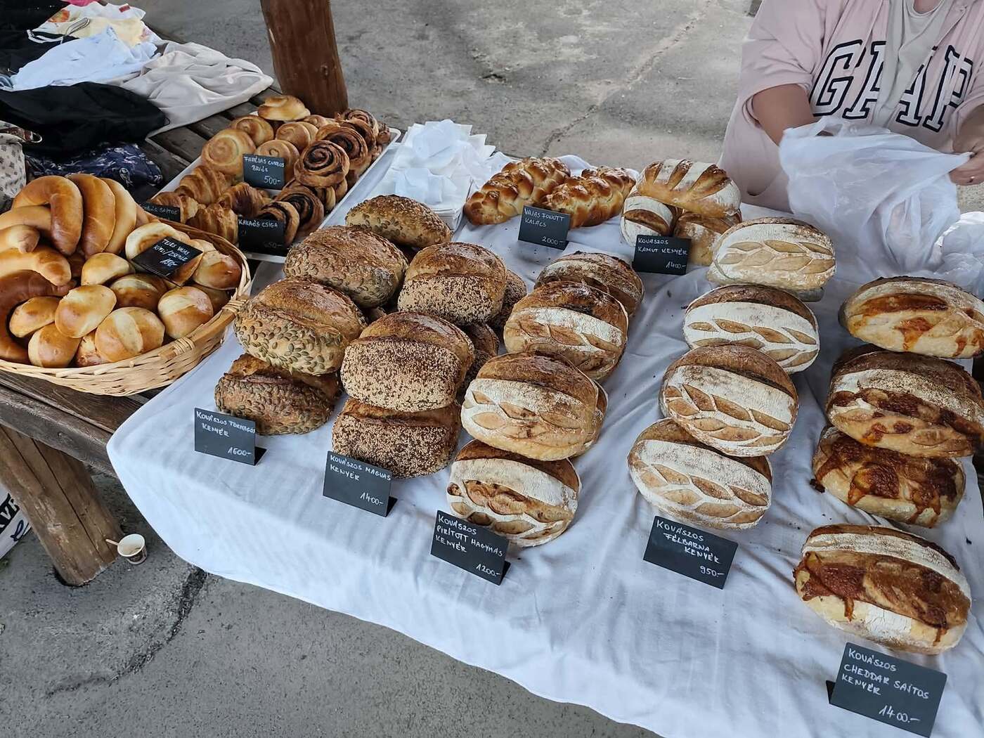 A pékség kínálata a piaci asztalon, kézzel írt ártáblákkal